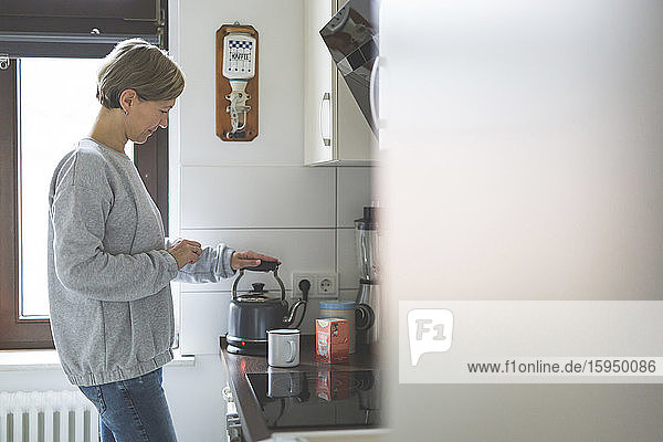 Mature woman preparing tea in kitchen
