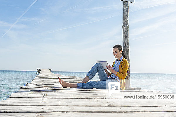 Frau sitzt mit digitalem Tablet am Steg  Mallorca  Spanien