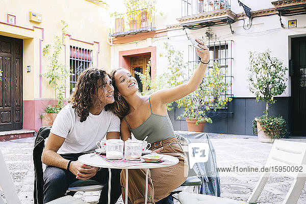 Junge Frau  die sich mit ihrem Freund per Mobiltelefon selbstständig macht  während sie in einem Straßencafé sitzt  Santa Cruz  Sevilla  Spanien