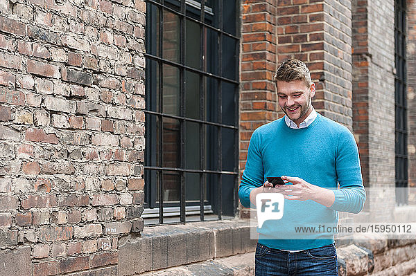 Smiling young businessman using smartphone at a brick building