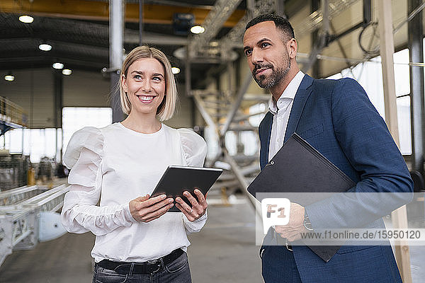Geschäftsmann und lächelnde junge Frau mit Tablette in einer Fabrik