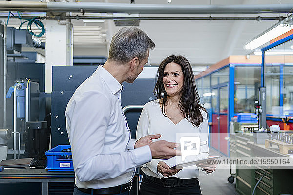 Geschäftsmann und Geschäftsfrau mit Produkt und Tablette bei einem Arbeitstreffen in einer Fabrik