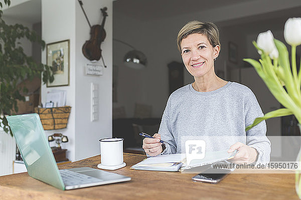Mature woman working from home  using laptop on table with flowers