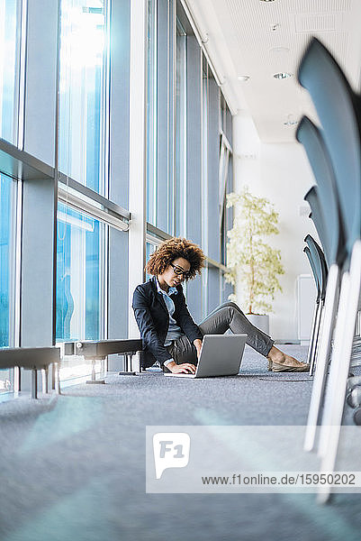 Junge Geschäftsfrau sitzt mit Laptop im Konferenzraum auf dem Boden