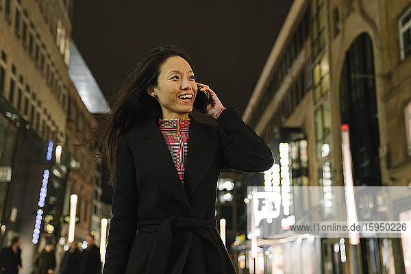 Happy young woman on the phone in the city at night  Frankfurt  Germany