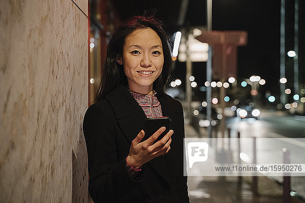 Porträt einer jungen Frau  die nachts in der Stadt ein Smartphone benutzt  Frankfurt  Deutschland