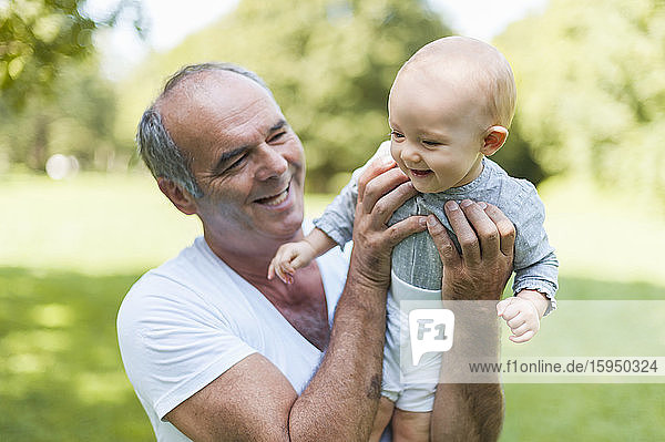 Smiling senior man holding baby girl in a park