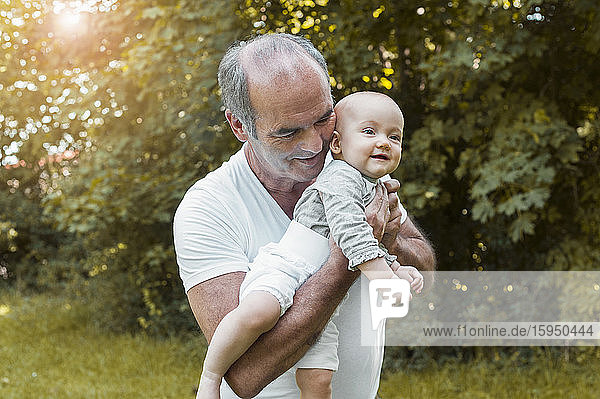 Smiling senior man holding baby girl on his arm in a park