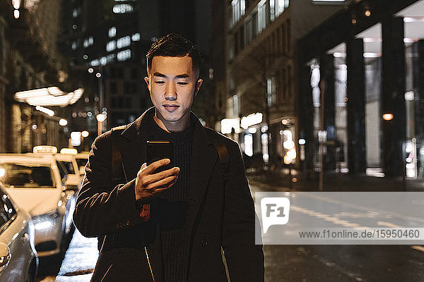 Man using smartphone while walking in the city at night