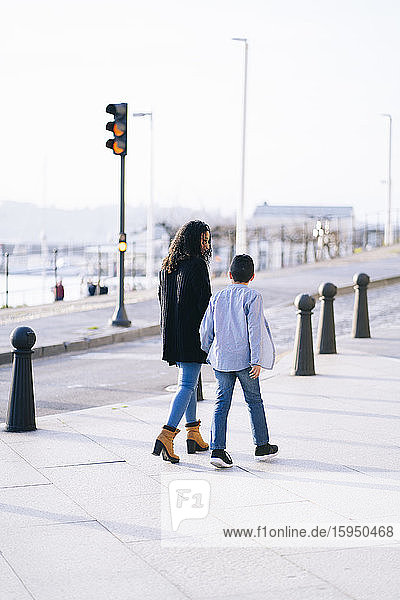 Rückenansicht von Mutter und Sohn beim Gehen auf dem Bürgersteig