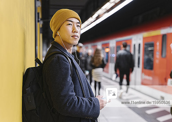 Stilvoller Mann mit gelbem Hut und Kopfhörern in der U-Bahn-Station