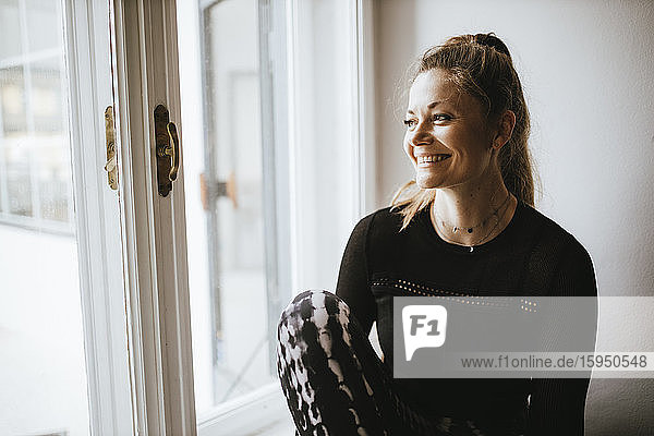 Lächelnde sportliche Frau auf dem Fensterbrett sitzend