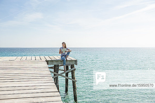 Woman sitting on jetty reading magazine  Mallorca  Spain
