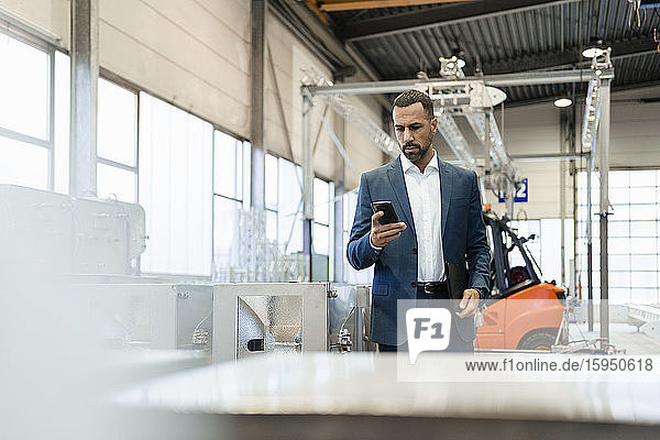 Businessman in a factory checking smartphone