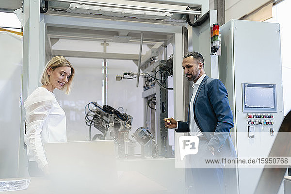 Geschäftsmann und junge Frau im Gespräch an einer Maschine in einer Fabrik