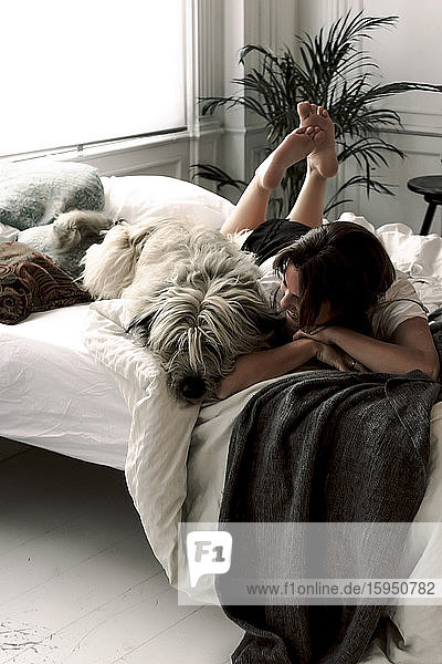 Reife Frau liegt mit ihrem Hund entspannt auf dem Bett