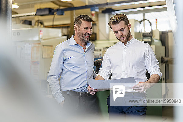 Zwei Männer diskutieren in einer Fabrik über einen Plan