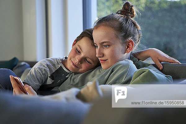 Bruder und Schwester sitzen zu Hause auf der Couch und benutzen ein Smartphone