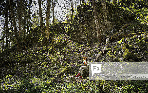 Girl sitting in Swabian Jura forest while using digital tablet during hiking weekend