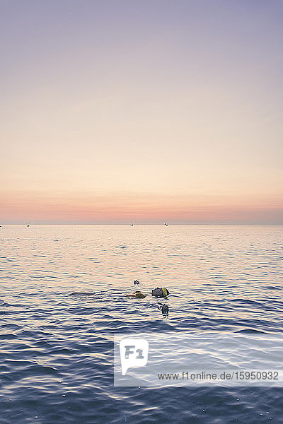 Teenage girl swimming in sea against sky during sunrise