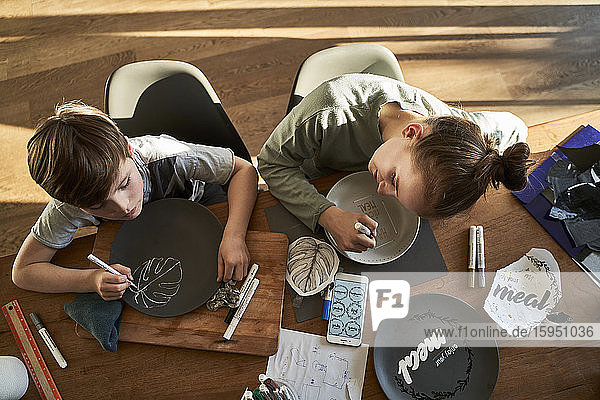 Brother and sister at home painting crockery with porcelain paint