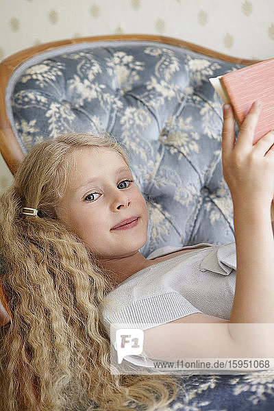 Porträt eines Mädchens  das auf einer Couch liegt und ein Buch liest