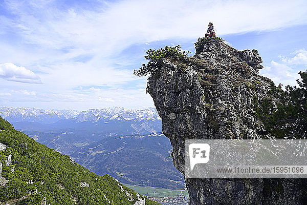 Weibliche Wanderin sitzt auf felsiger Bergspitze und betrachtet Landschaft gegen den Himmel