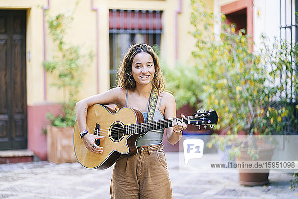 Porträt einer lächelnden jungen Frau  die Gitarre spielt  während sie auf der Straße steht  Santa Cruz  Sevilla  Spanien