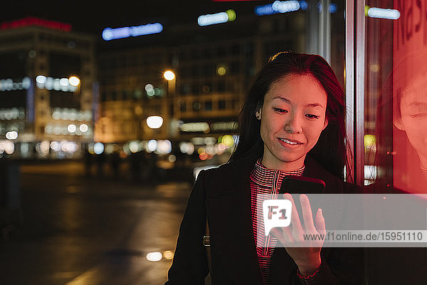 Young woman using smartphone in the city at night  Frankfurt  Germany
