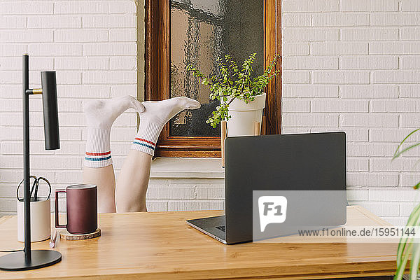 Gelangweilte Frau mit erhobenen Füßen am Laptop am Tisch im Home-Office