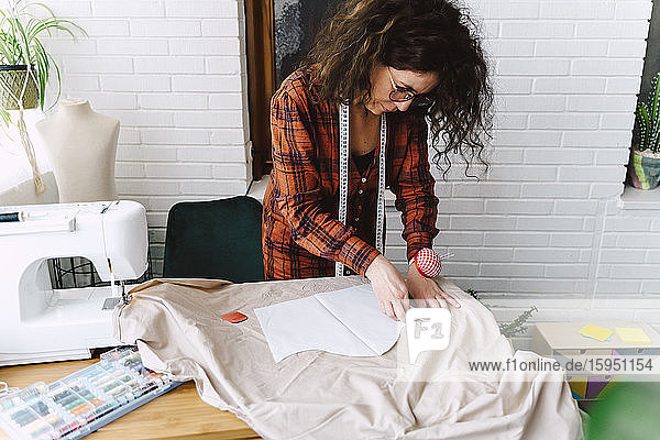 Woman pinning sewing pattern on table at home