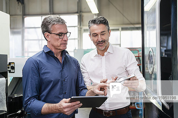 Geschäftsleute in einer Fabrik  die eine Besprechung abhalten und ein digitales Tablett verwenden