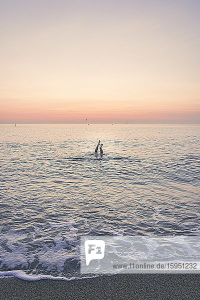 Teenager-Mädchen schwimmt bei Sonnenaufgang im Meer mit den Füßen gegen den Himmel