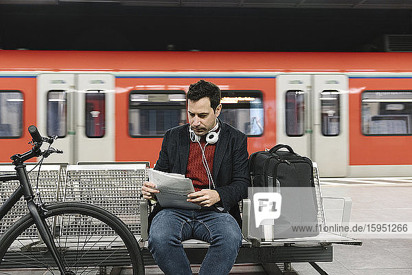 Businessman with bicycle reading documents while sitting at metro station  Frankfurt  Germany