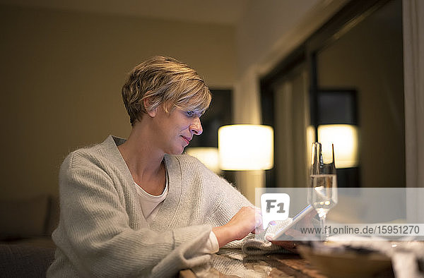 Blonde Frau arbeitet spät  während sie ein digitales Tablet im beleuchteten Wohnzimmer benutzt