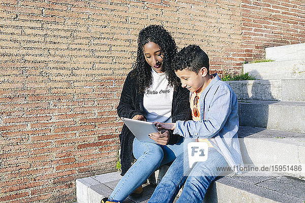 Mutter und Sohn sitzen gemeinsam auf einer Treppe und benutzen ein digitales Tablett