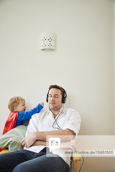 Junge im Superman-Kostüm und nervender Vater beim Musikhören mit Kopfhörern