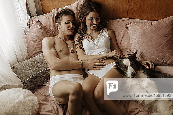 Glückliches junges Paar und Hund liegen im Bett