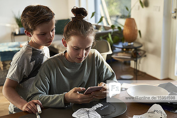 Brother and sister at home using smartphone for a creative online tutorial
