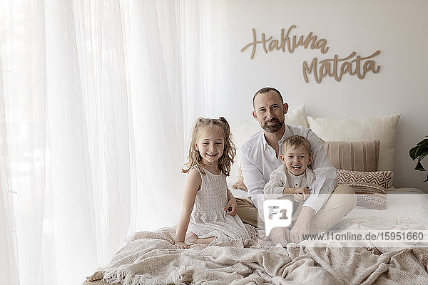 Familienporträt eines glücklichen Vaters und seiner zwei Kinder  die zusammen auf dem Bett sitzen