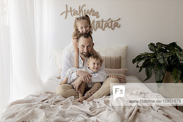 Familienporträt eines glücklichen Vaters  der mit seinen beiden Kindern im Bett sitzt