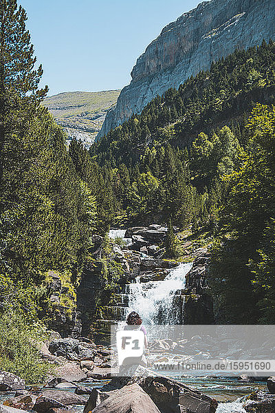 Spanien  Provinz Huesca  Wanderin bewundert kleinen Wasserfall am klaren Bergfluss