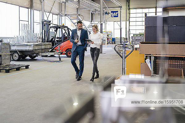 Businessman and young woman with tablet walking and talking in a factory