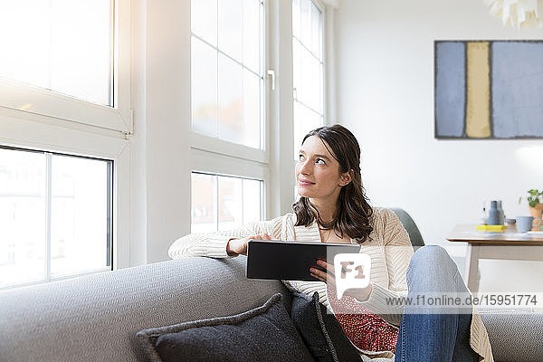 Frau sitzt zu Hause auf Couch mit Tablette