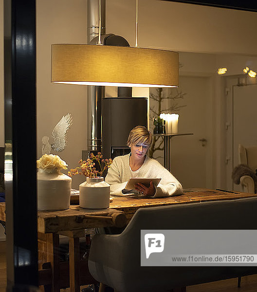 Frau  die zu Hause mit einem digitalen Tablet arbeitet  während sie im Wohnzimmer am Tisch sitzt