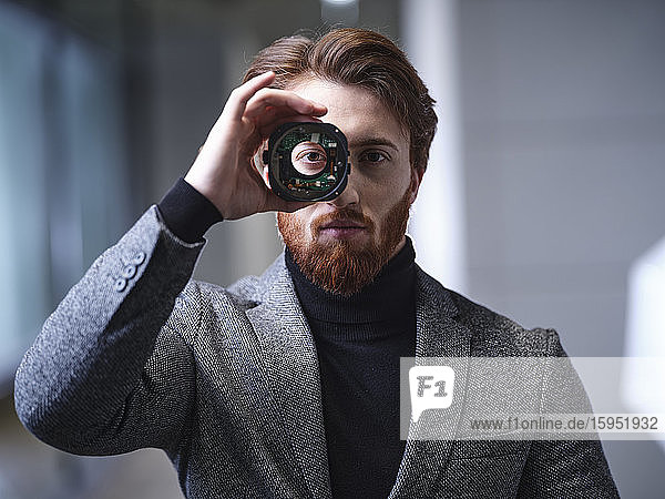 Portrait of businessman looking through an object in modern office