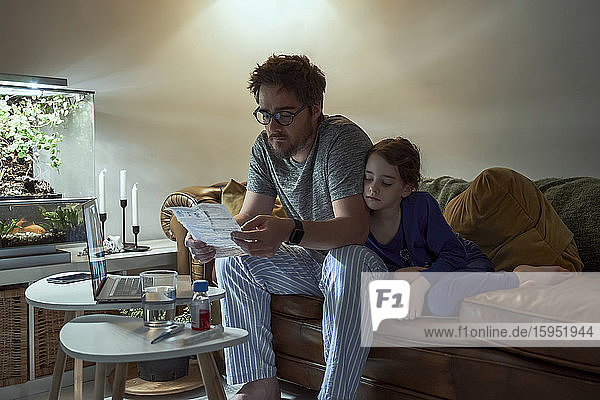 Mann bespricht Verschreibung mit Arzt über Videoanruf  während er bei seiner Tochter zu Hause im Wohnzimmer sitzt