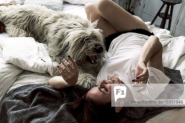 Mature woman lying on bed playing with her dog