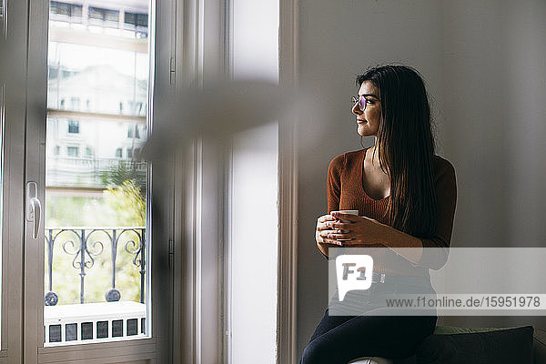 Thoughtful looking through window while enjoying coffee at office during break