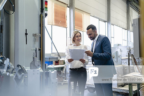Businessman and young woman with papers talking at a machine in a factory
